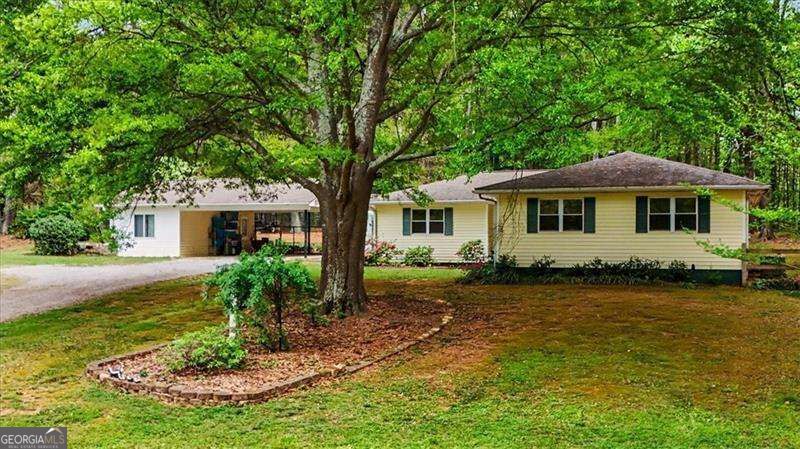 Single-story ranch home beneath a large shade tree, with a covered porch and lawn.