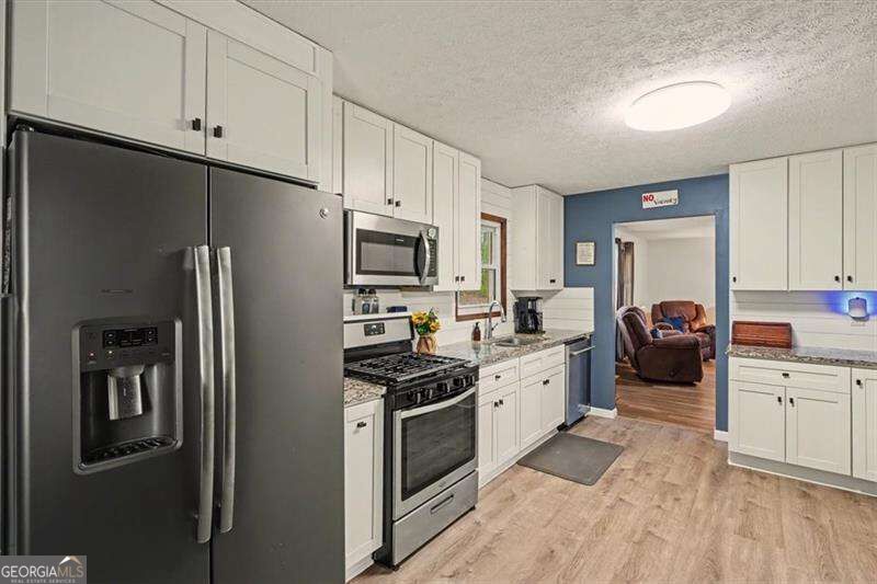 Kitchen with white cabinetry, stainless steel appliances, and a blue accent wall beside the doorway.