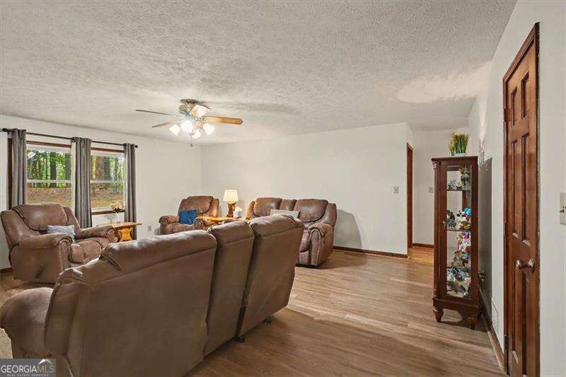 Living room with brown leather seating, wood-look floors, curtained windows, and a ceiling fan.