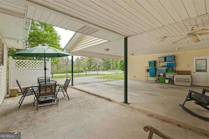 Covered concrete patio with outdoor dining set, green umbrella, ceiling fan, and storage shelving.