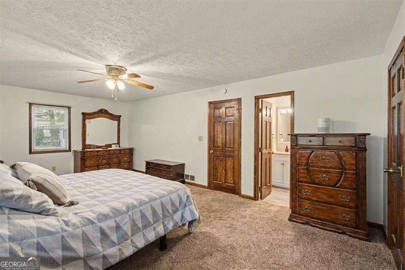 Furnished bedroom with a patterned bed, dark wood dressers, and an open doorway to the bathroom.
