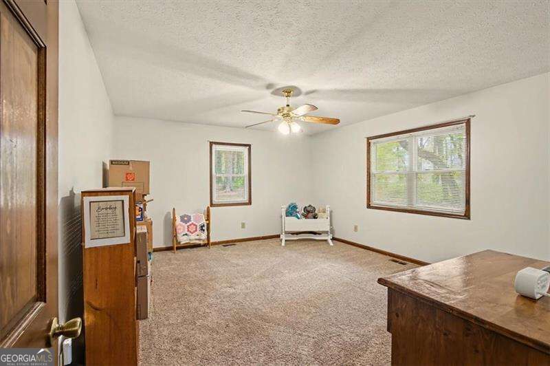 Carpeted room with a ceiling fan, two windows, and a few pieces of furniture.