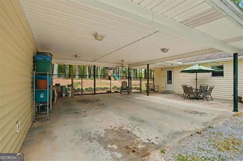 Covered concrete patio with support posts, outdoor dining set, and green umbrella beside a house.