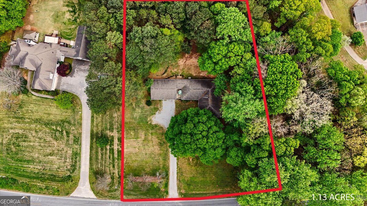 Aerial view of a wooded 1.13-acre property with a house, driveway, and red boundary outline.