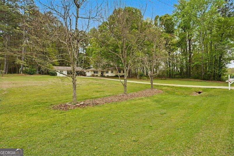 Single-story home beyond a broad lawn, framed by mature trees and a paved driveway.