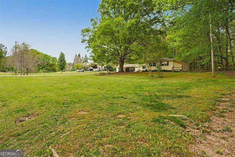 Single-story home beyond a broad lawn, partly screened by a large leafy tree.