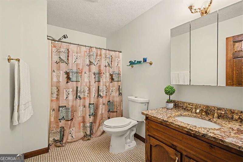 Bathroom with a granite-topped wood vanity, mirrored cabinet, and patterned shower curtain.