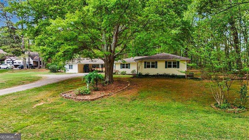 Single-story ranch home beneath a large leafy tree, with a lawn and curving driveway.