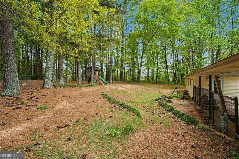Wooded backyard with a children's playset and the side of the house.