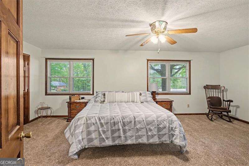Bedroom with a gray geometric quilt, two windows, and a wooden rocking chair.