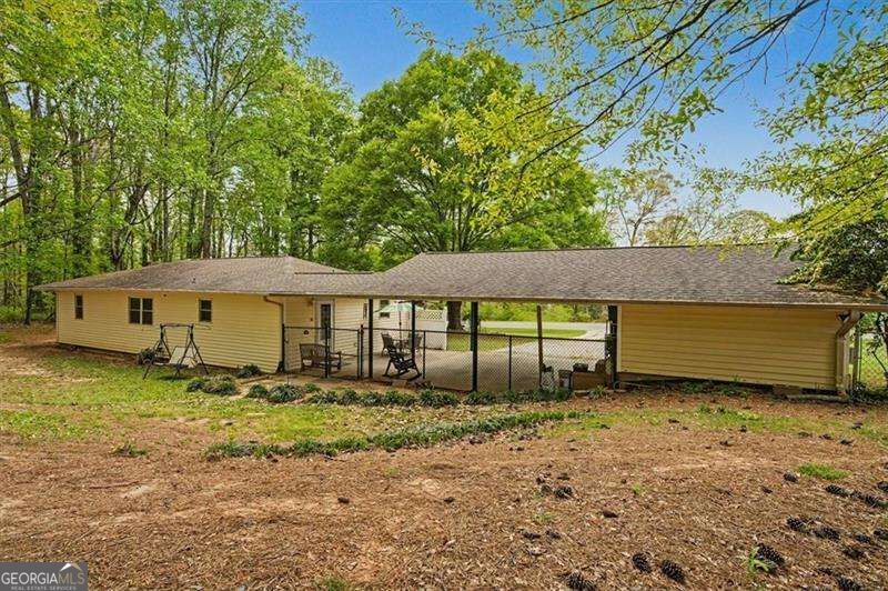Rear of a yellow home with a long fenced, covered patio beside a wooded yard.