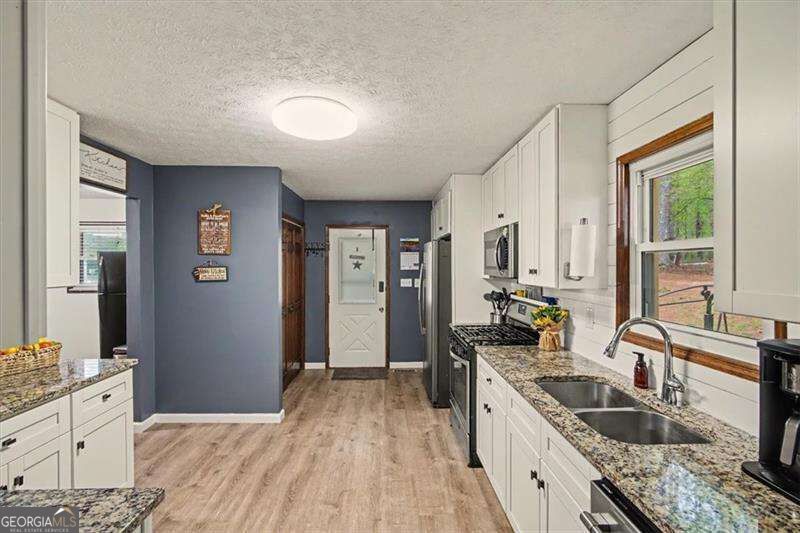 Kitchen with white cabinets, granite counters, stainless appliances, and a double sink beneath a window.