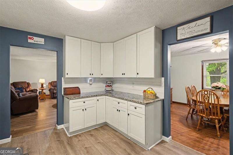 Kitchen with white cabinets and granite counters, opening to furnished living and dining rooms.