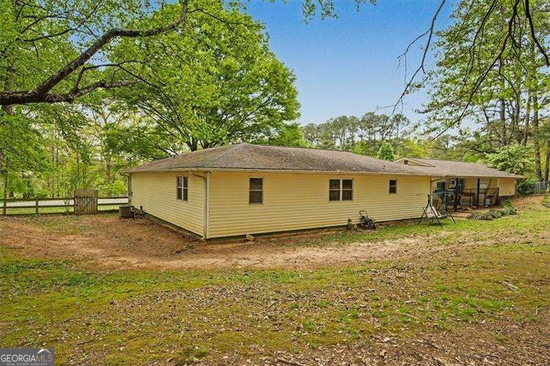 Single-story beige house with a fenced wooded yard and outdoor seating area.