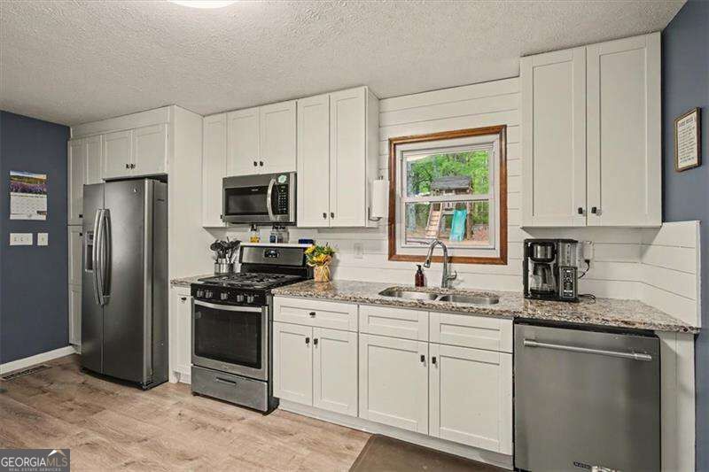 Kitchen with white cabinets, granite counters, stainless steel appliances, and a window above the sink.