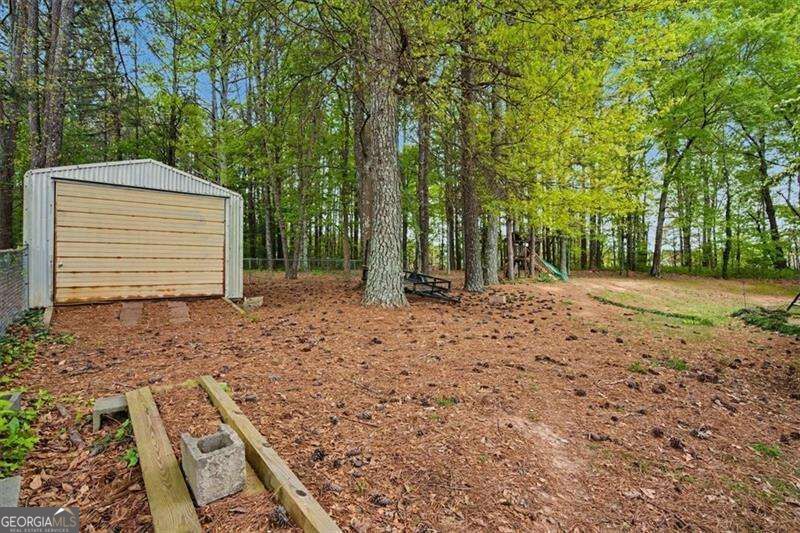Wooded backyard with a small shed and wooden play equipment beneath mature trees.