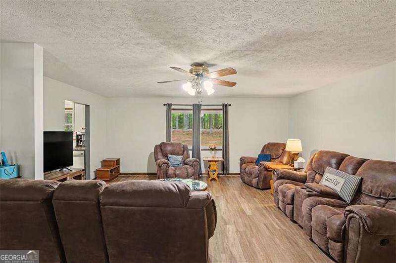 Furnished living room with brown reclining sofas, wood-look flooring, and a window overlooking trees.