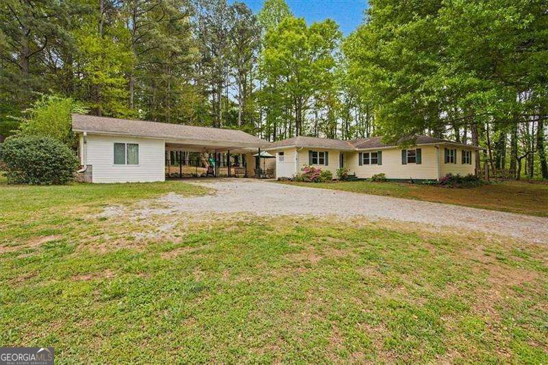 Single-story ranch home with a covered carport and gravel driveway, surrounded by mature trees.