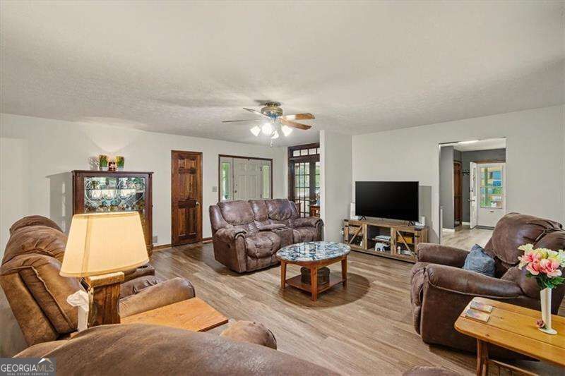 Furnished living room with brown leather seating, wood-look floors, and a glass-topped coffee table.
