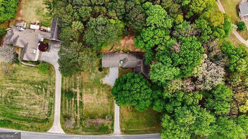 Aerial view of a wooded property with a house, outbuilding, and long driveway.