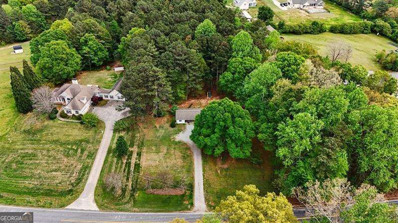 Aerial view of a house and wooded property with a long driveway and open lawn.