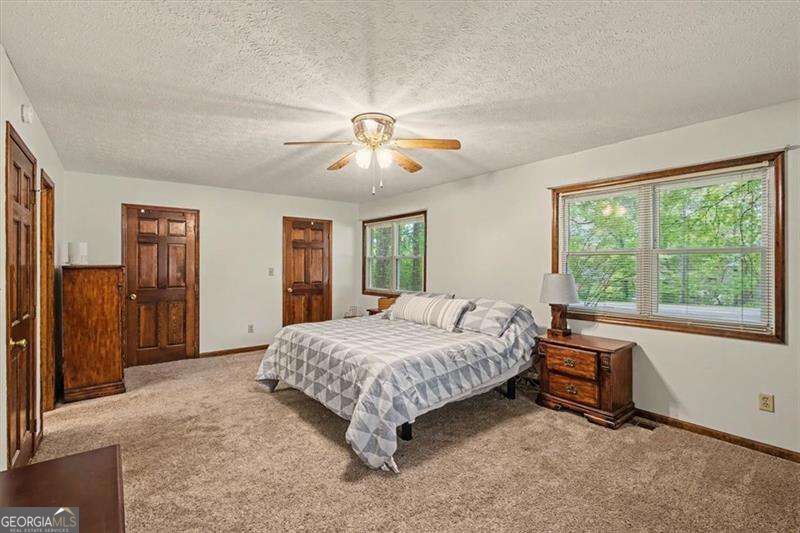 Bedroom with a bed, ceiling fan, and wood-trimmed windows overlooking trees.