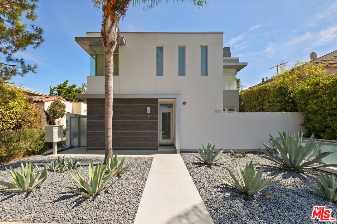 Modern two-story home with a white facade, dark entry wall, and gravel landscaping planted with agaves.