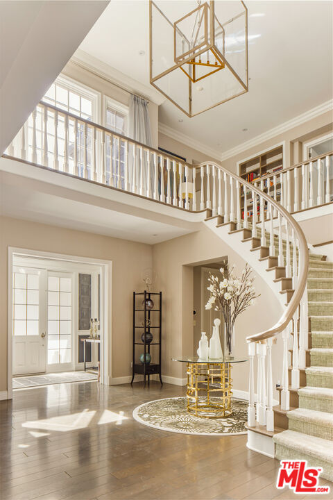 Double-height foyer with a curved staircase, geometric chandelier, and glass-topped console table.