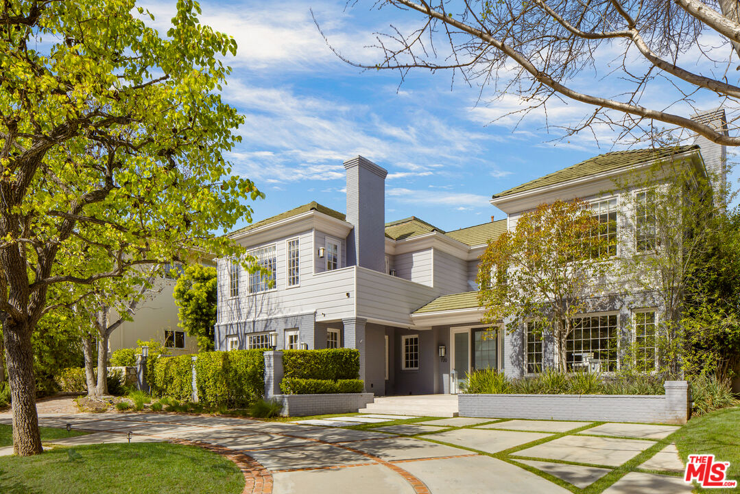 Two-story light-sided house with a tall chimney, broad windows, and landscaped front yard.