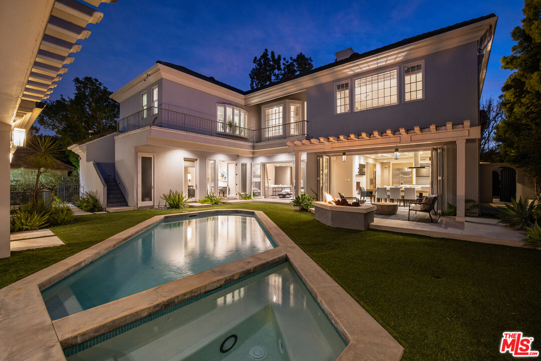 Two-story home at twilight with a swimming pool and illuminated covered patio.
