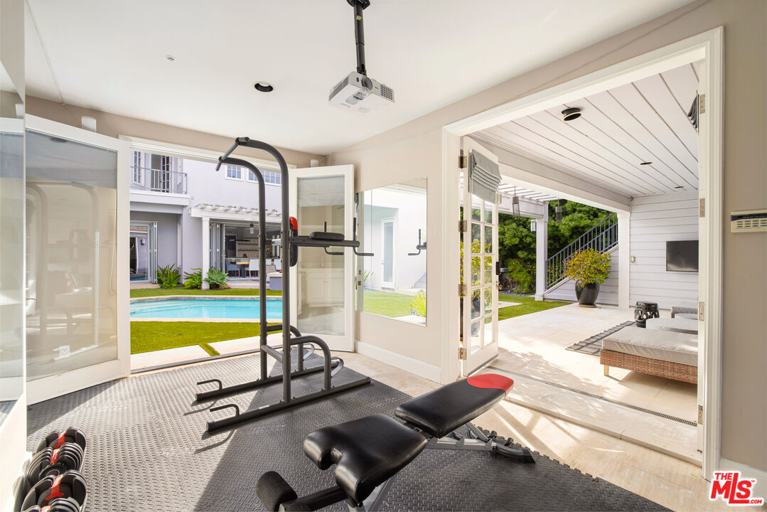 Home gym with weight equipment and open glass doors overlooking a swimming pool and patio.