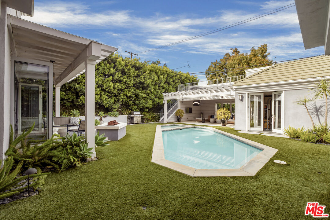 Backyard swimming pool surrounded by lawn, covered patios, outdoor seating, and mature landscaping.