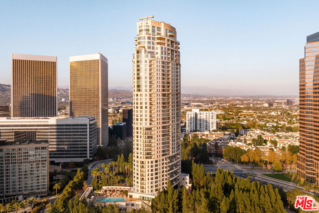 High-rise condominium tower among Century City skyscrapers, with Los Angeles and distant hills beyond.
