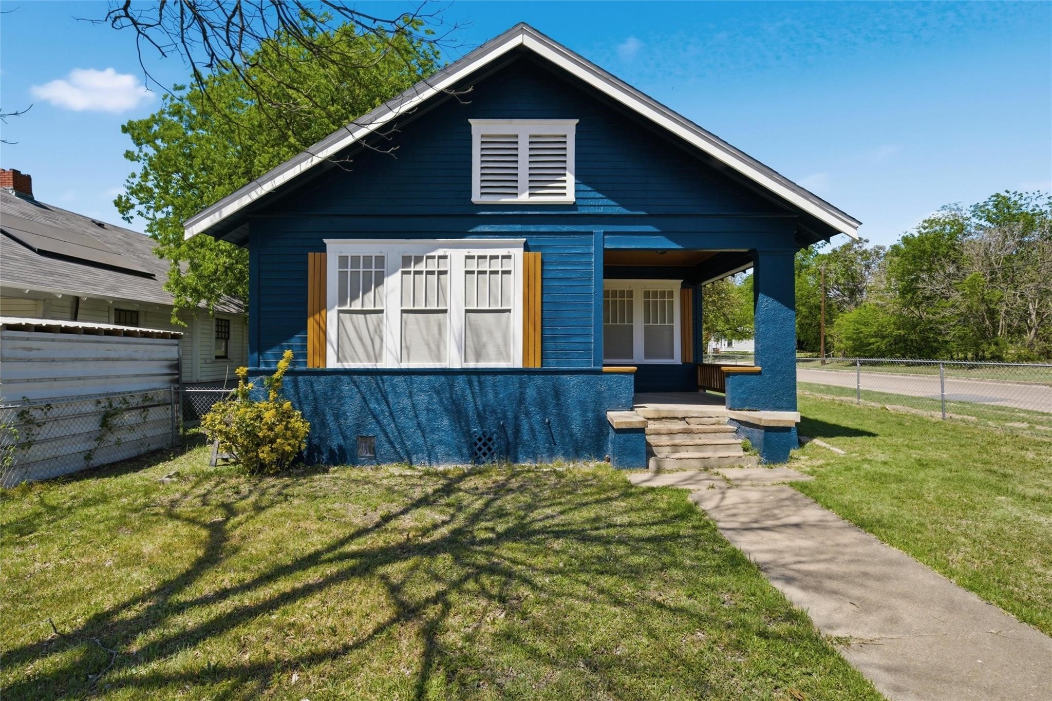 Blue bungalow with white trim, mustard shutters, and a covered front porch.
