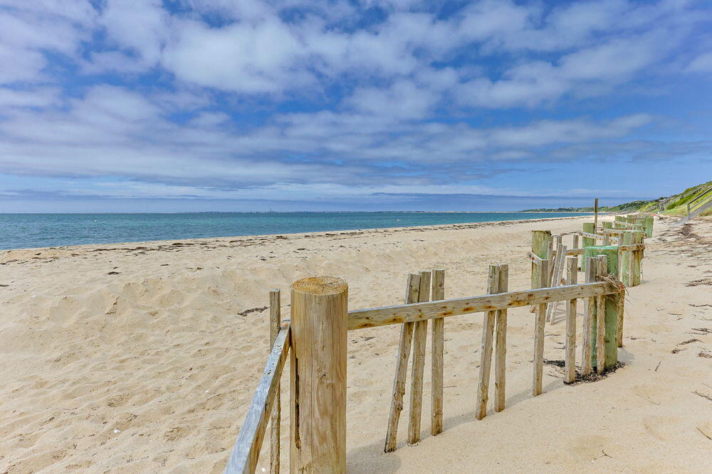 Sandy beach and blue water beside a weathered wooden dune fence.