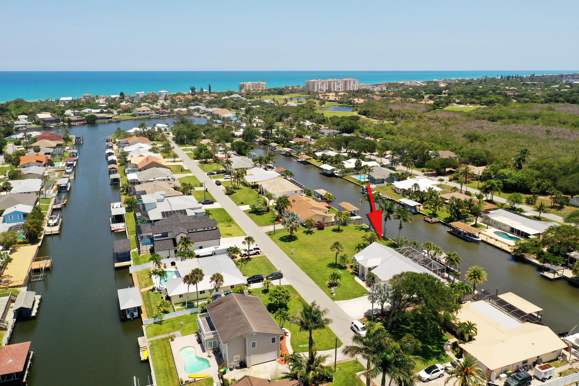 Aerial view of a canal-front home marked by a red arrow, with the ocean beyond.
