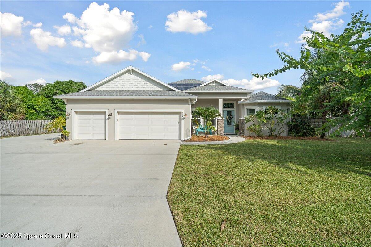Single-story light-colored house with two garage doors, a broad driveway, and a landscaped lawn.