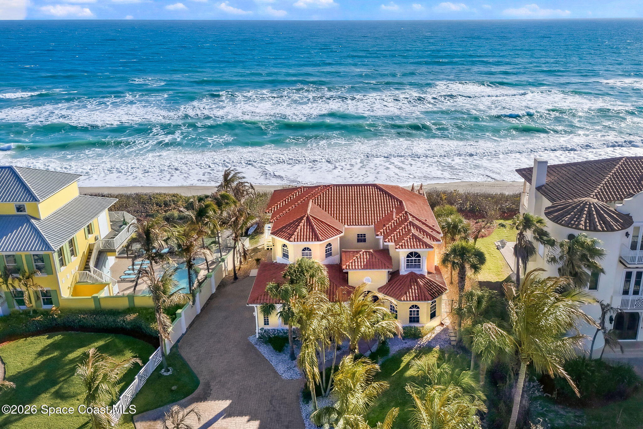 Aerial view of a red-roofed coastal home beside the ocean and neighboring beach houses.