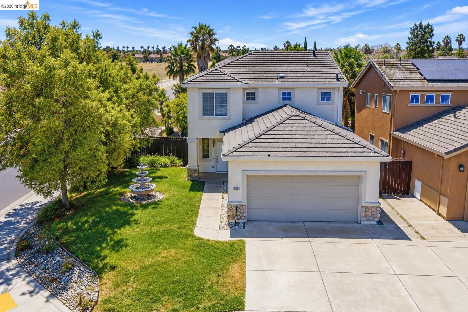 Two-story house with a gray tile roof, wide driveway, and landscaped front lawn with a fountain.