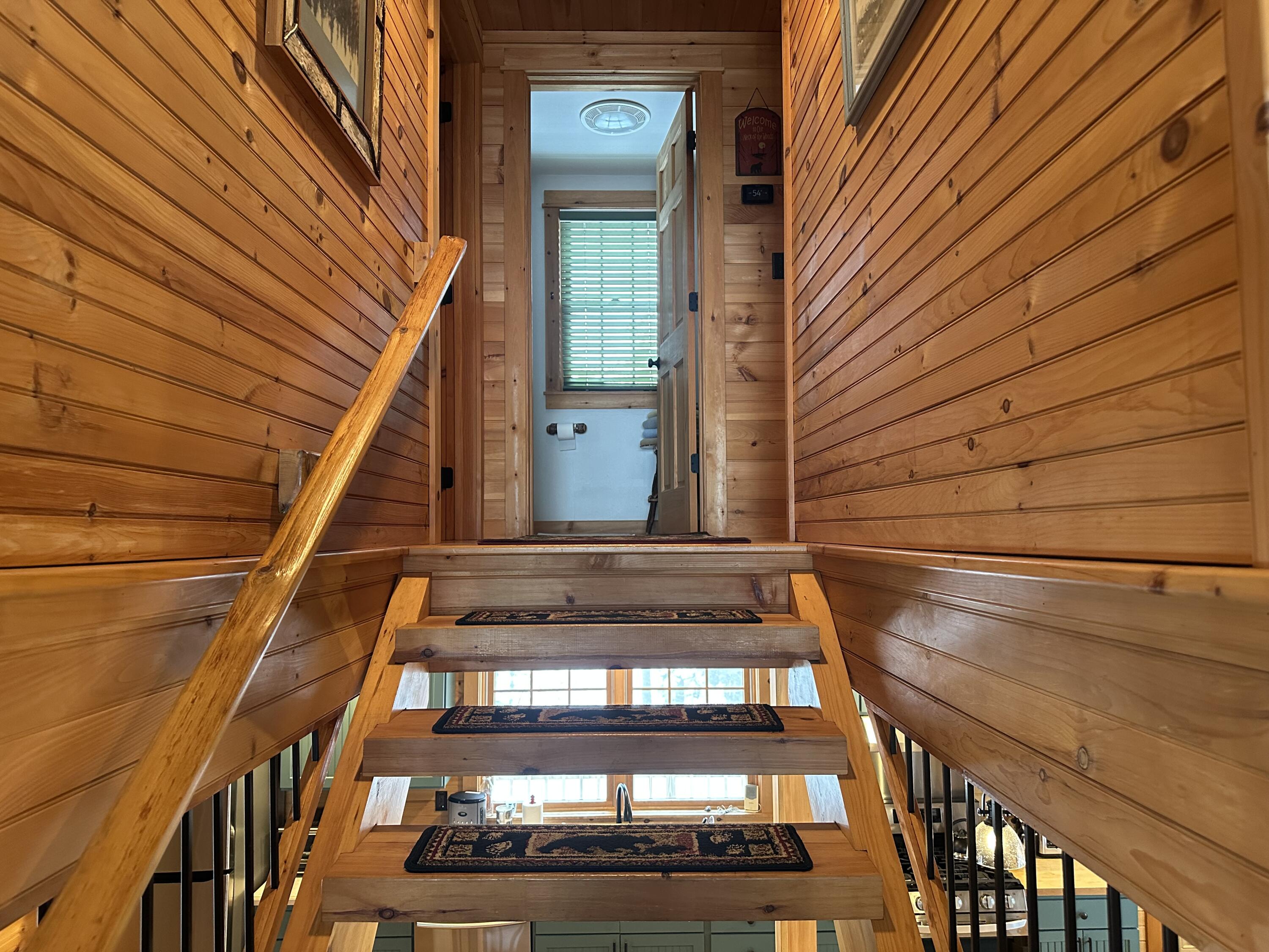 Wooden staircase with open risers and patterned runners, leading to a bathroom doorway above the kitchen.