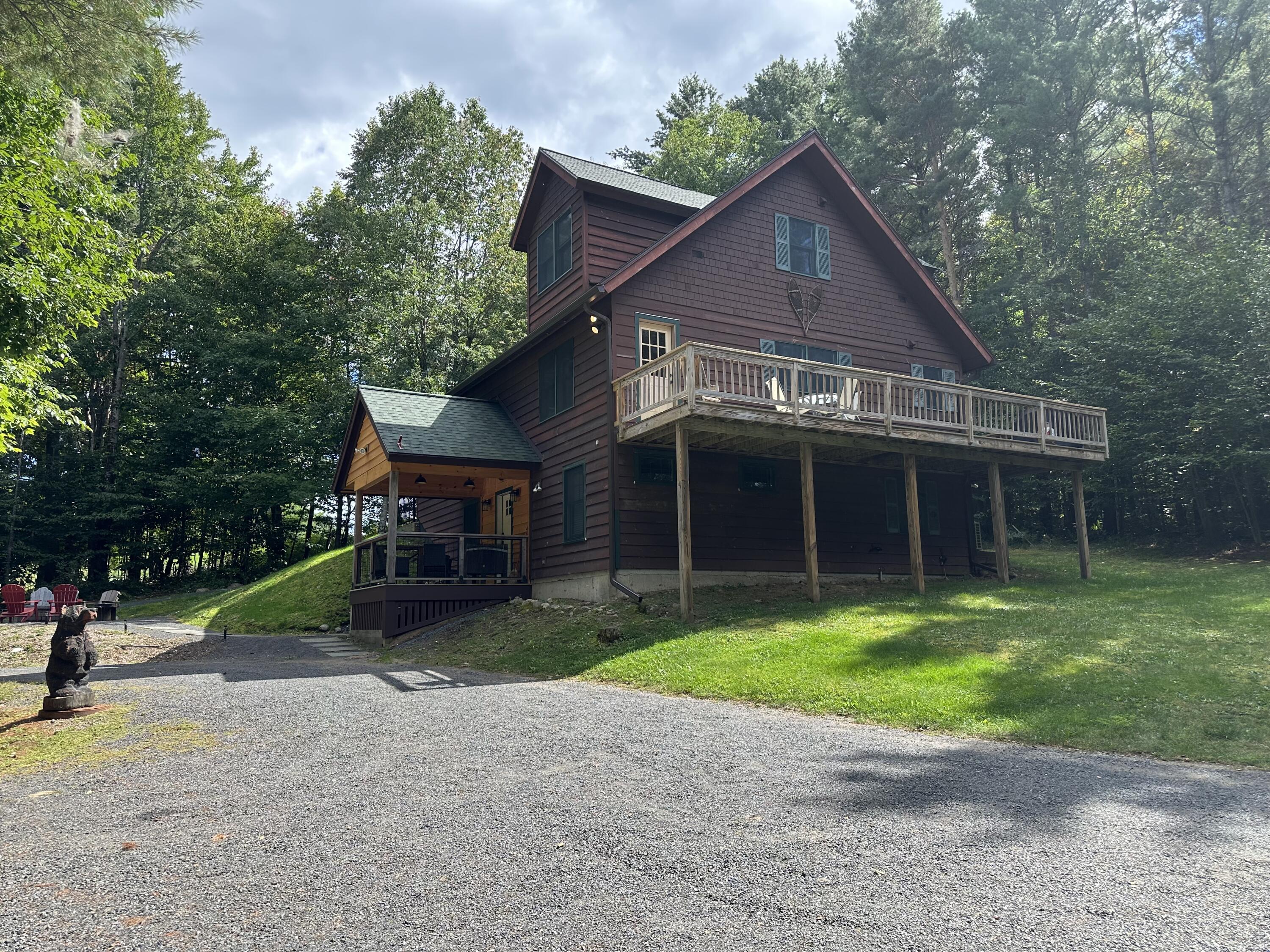 Wood-sided home with a long elevated deck, covered porch, and wooded surroundings.