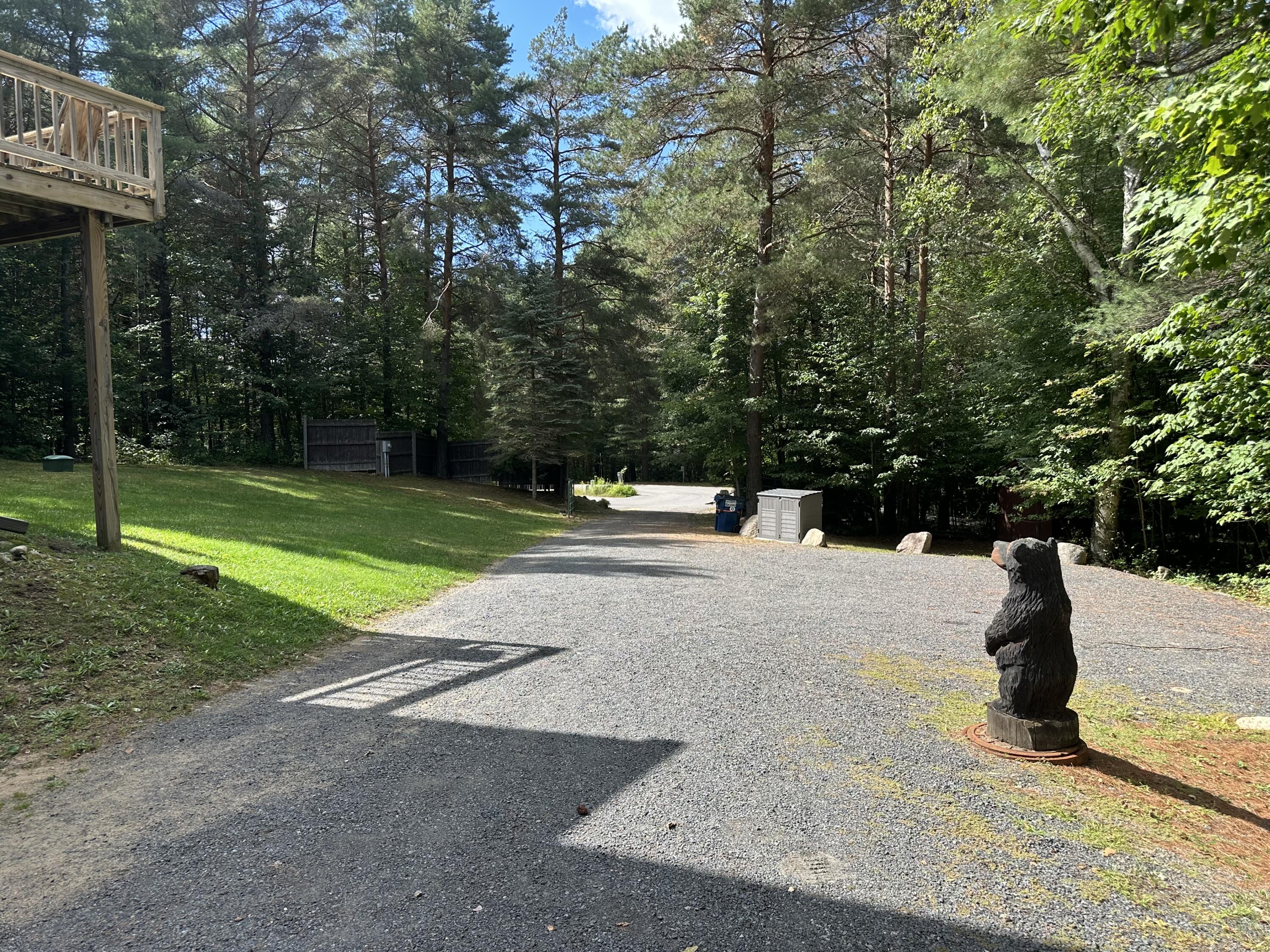 Gravel driveway through woods, with a raised deck and carved bear statue.