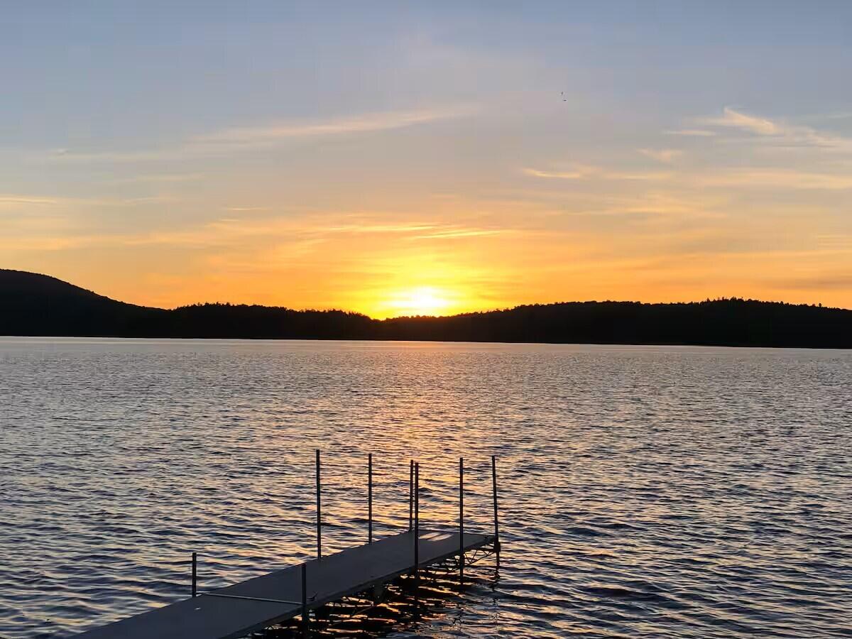 Lake at sunset with a dock extending into rippling water and wooded hills along the horizon.