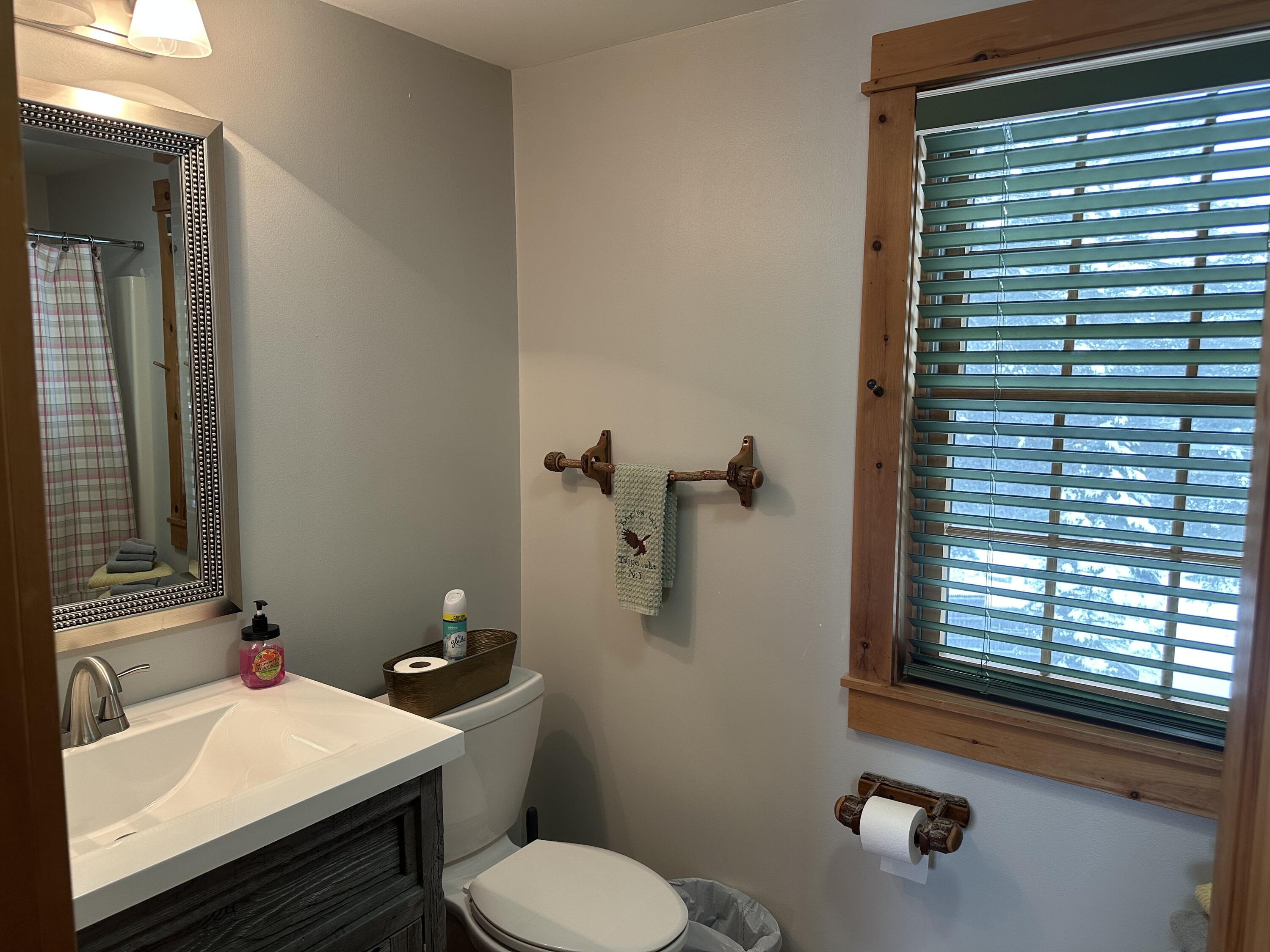 Bathroom with a dark wood vanity, framed mirror, and large wood-trimmed window with blinds.