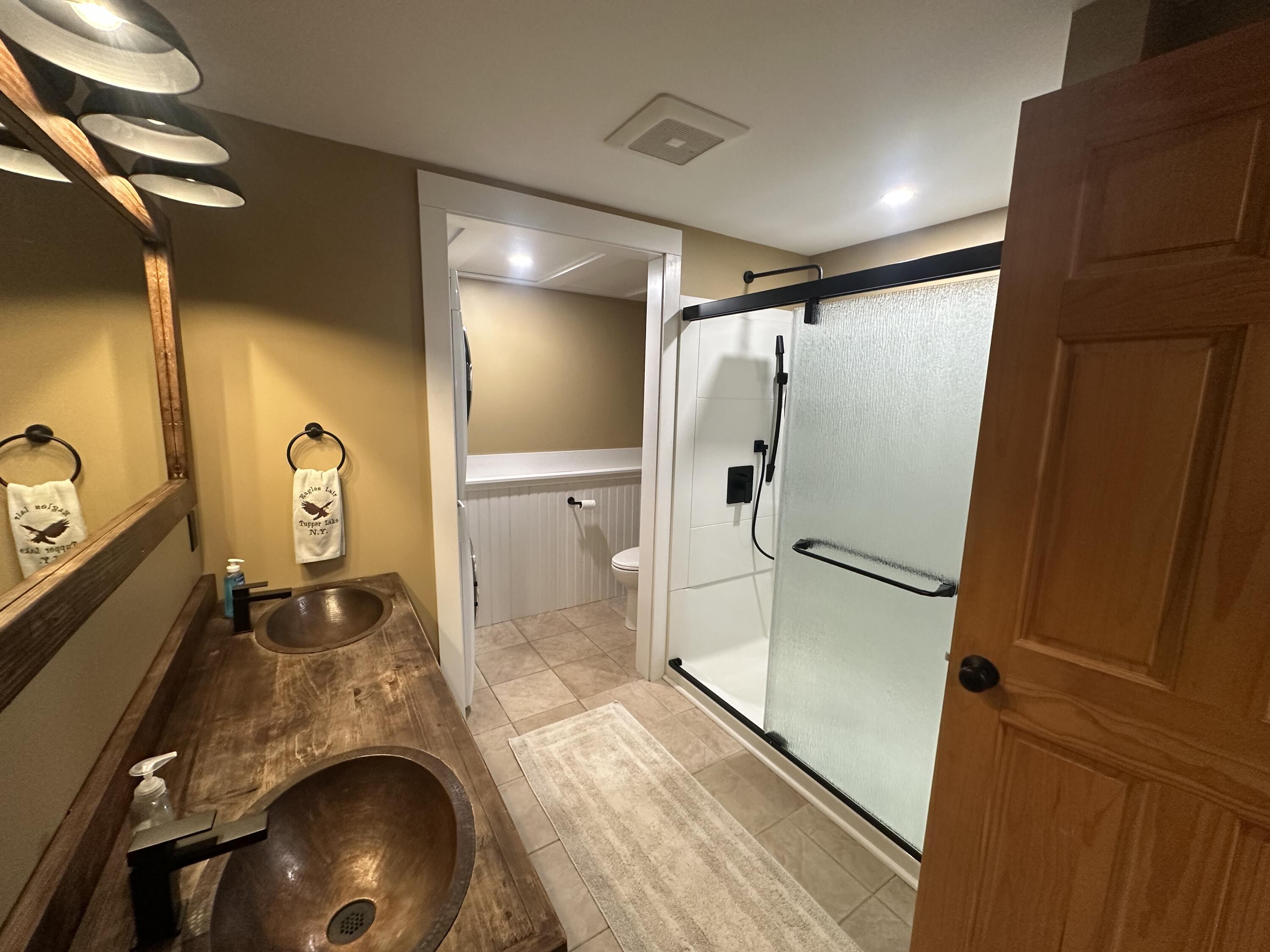 Bathroom with a rustic double copper-sink vanity and a tiled walk-in shower behind frosted glass.