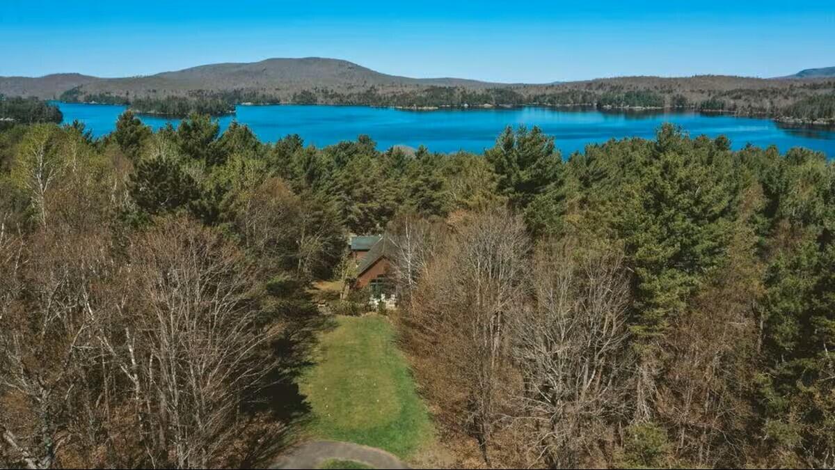 Aerial view of a wooded cabin beside a blue lake, with hills on the far shore.