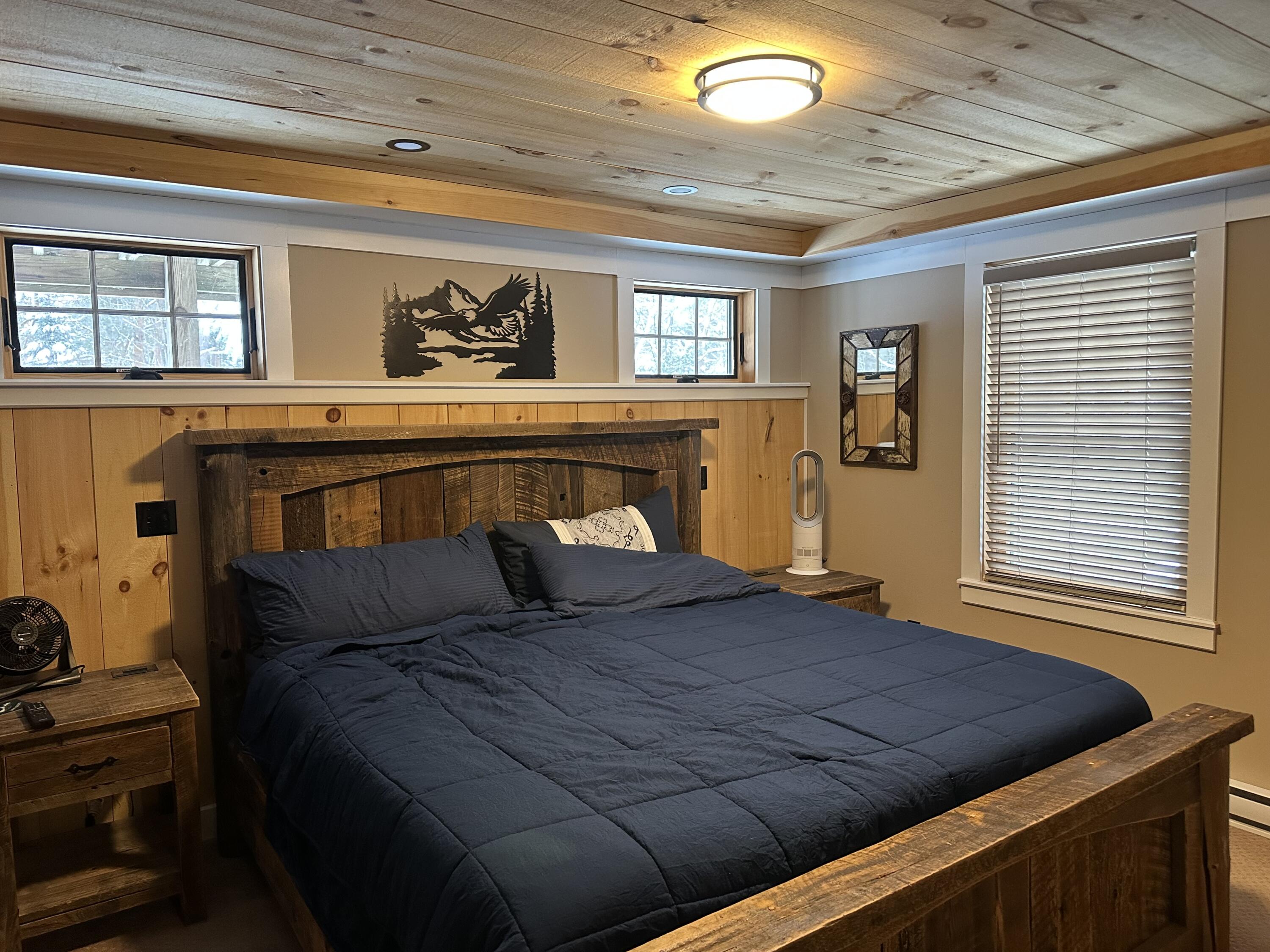 Bedroom with a rustic wooden bed, navy bedding, and a plank wood ceiling.