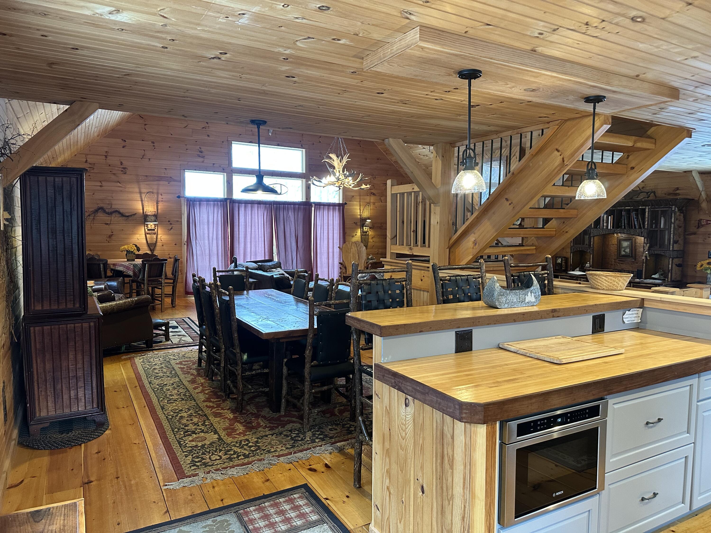 Rustic kitchen and dining area with a large island, long dining table, and open timber staircase.