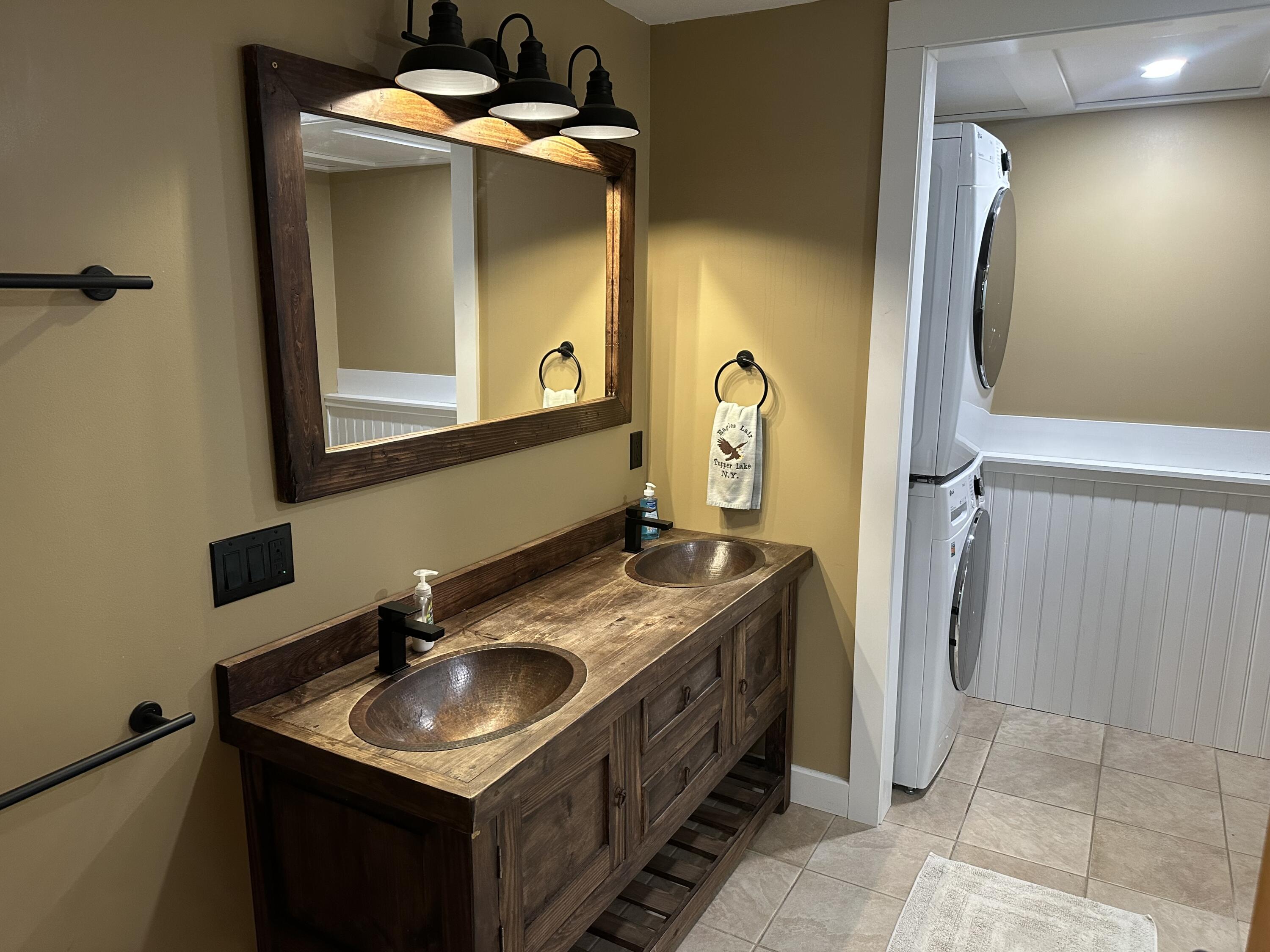 Bathroom with a rustic double vanity, copper sinks, and a stacked washer and dryer.