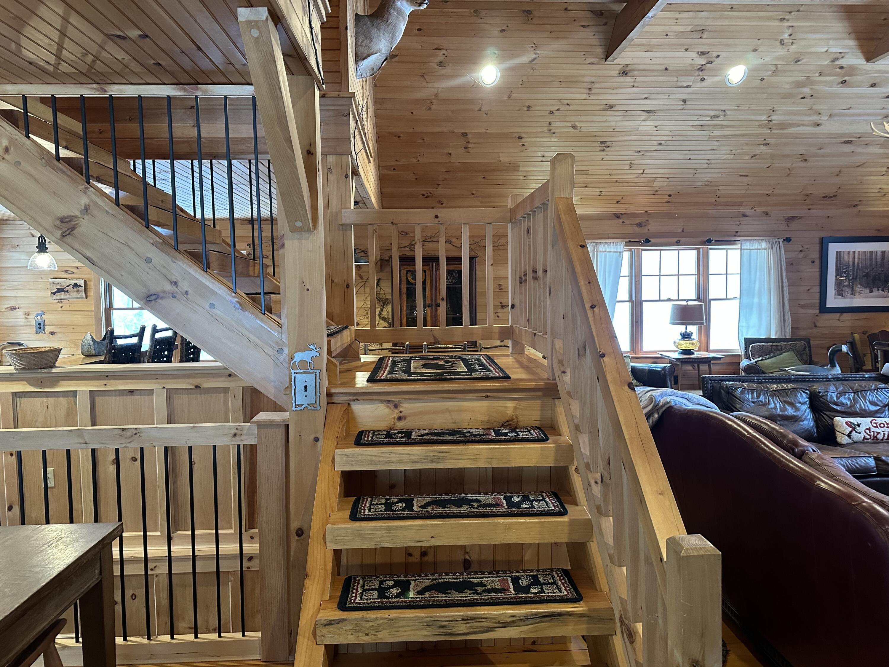 Timber staircase with patterned runners in a wood-paneled home, beside a leather-furnished living area.